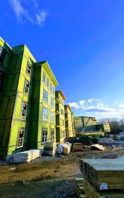 Four-story apartment building framed and sheathed with windows being installed on a large multifamily construction site